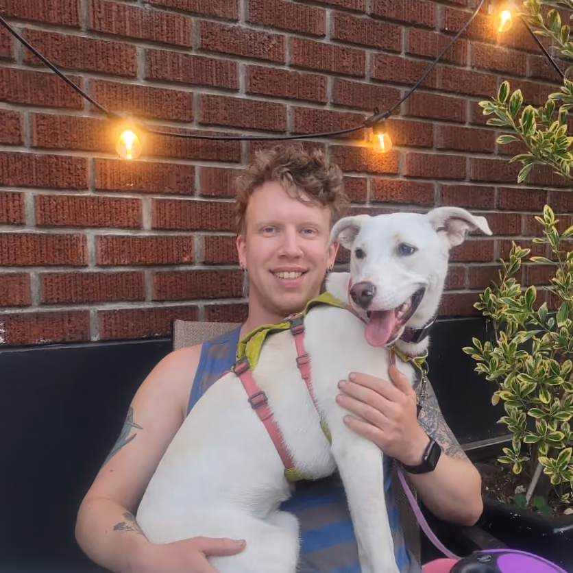 Colter Garrison holding his white dog Ožujsko under string lights